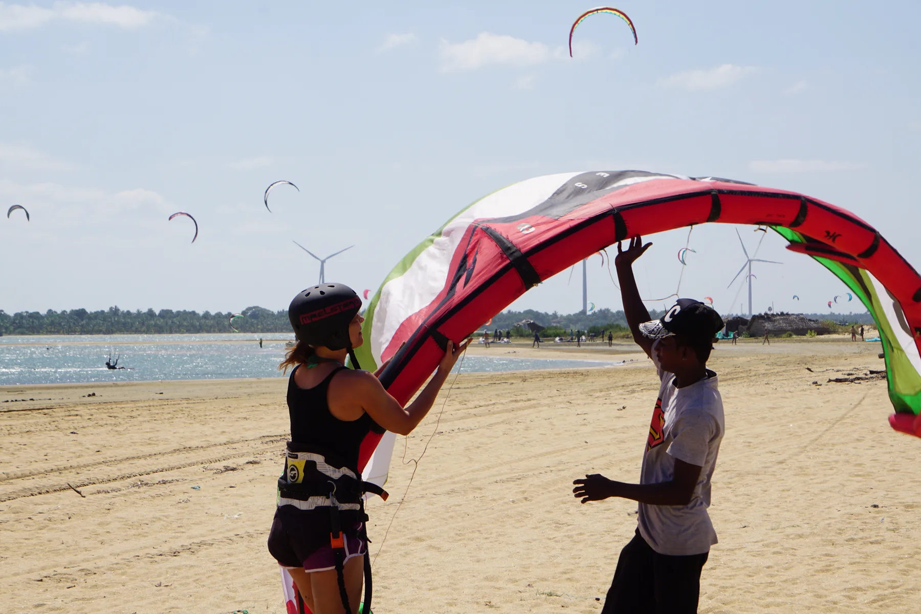 Instructor and student launching a kite together on the beach at Kalpitiya, windmills and lagoon behind