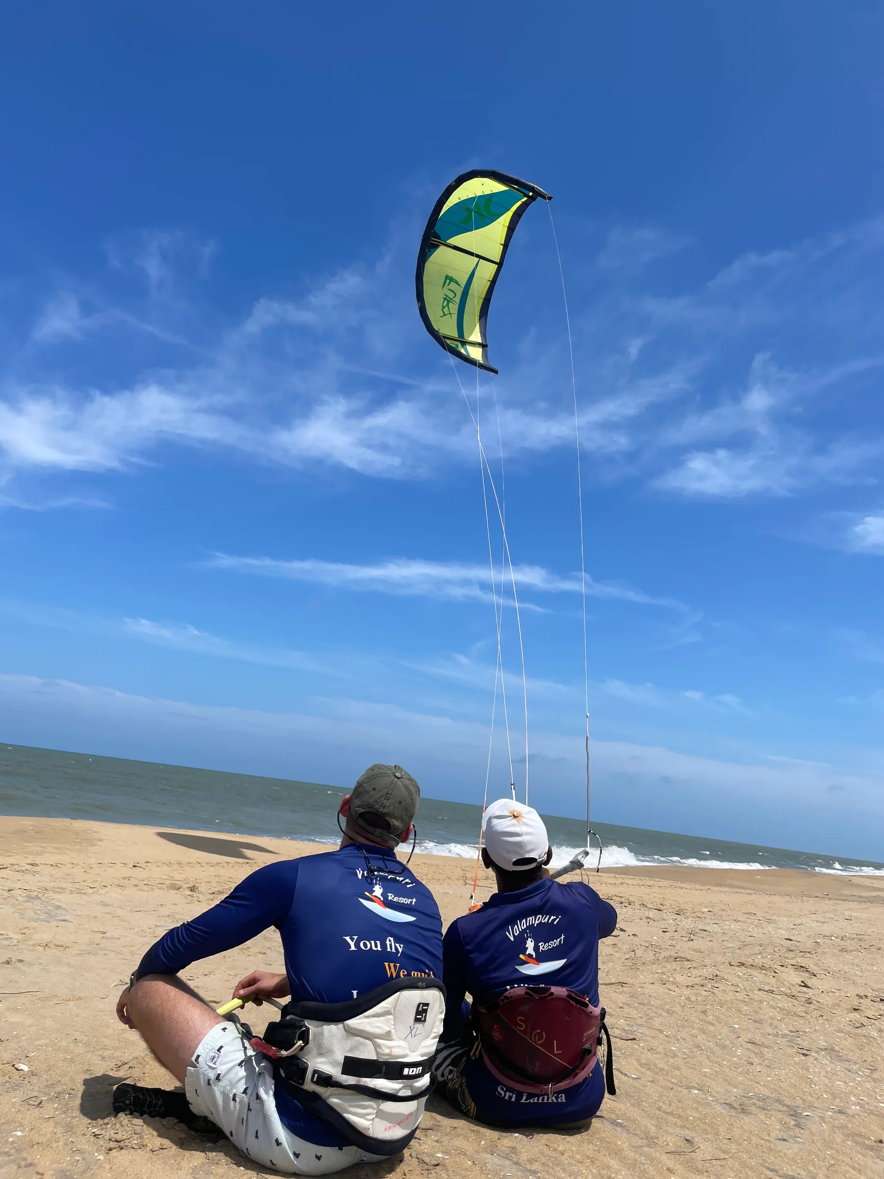 Valampuri instructor and student sitting on the beach watching a kite fly, learning kite control at Kalpitiya