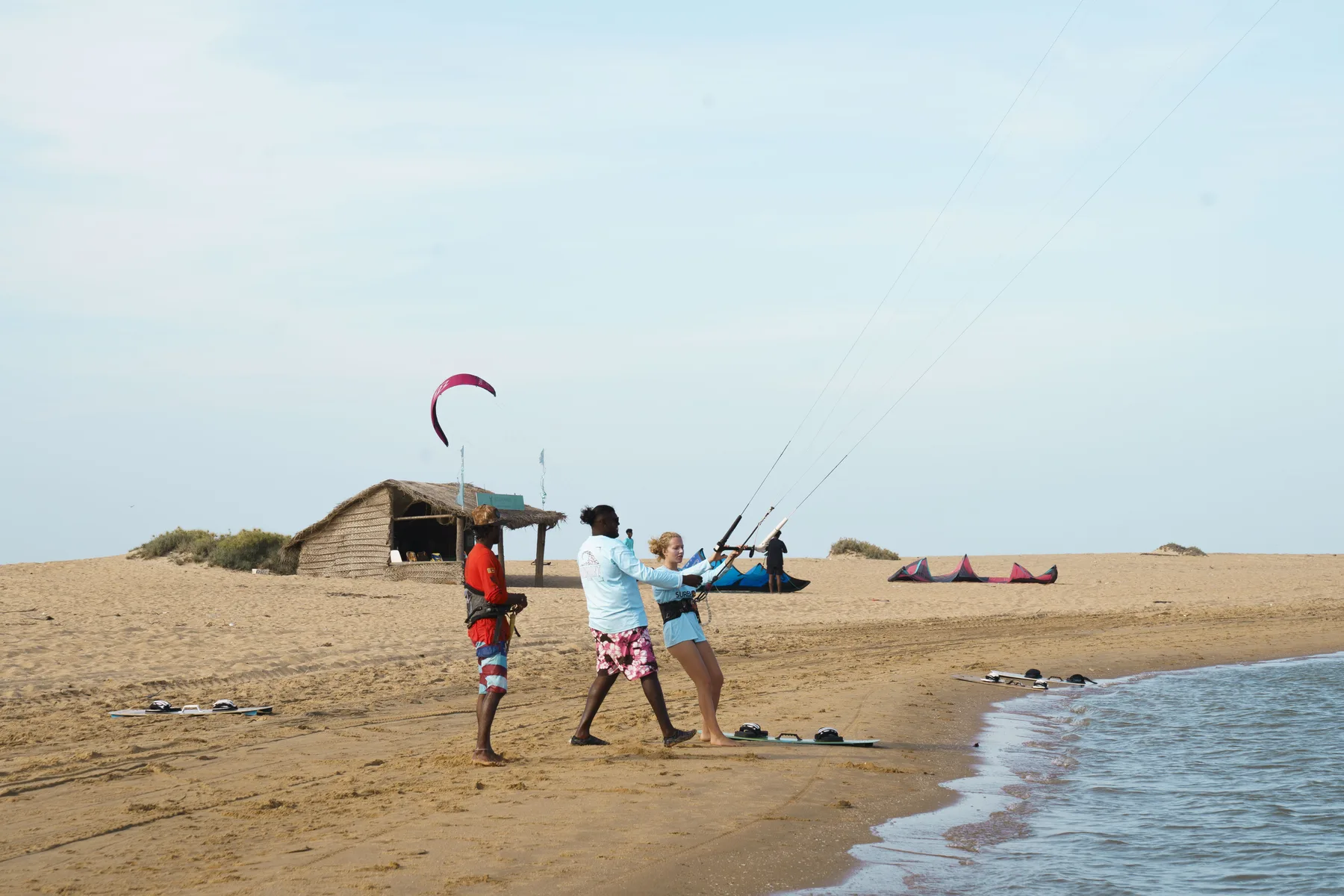 Two instructors coaching a beginner at the water's edge in Kalpitiya, boards and kites ready on the sand